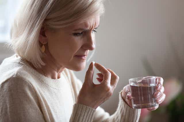 woman looks concerned, about to take pill with water
