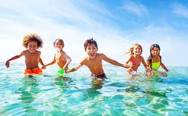 Niños riendo cogidos de la mano en el agua en la playa.