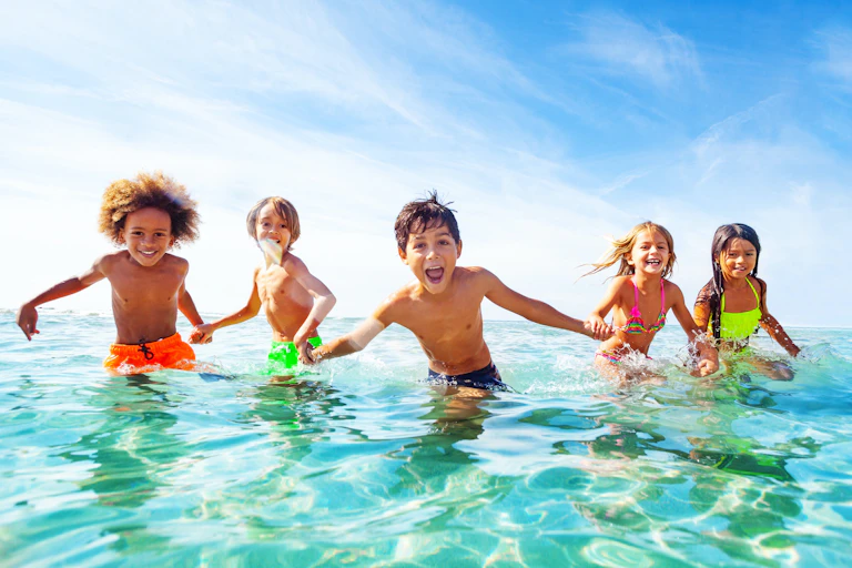 Niños riendo cogidos de la mano en el agua en la playa.