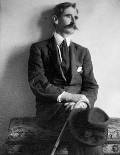 A black-and-white photo of a thoughtful man in a suit, with a moustache and cane