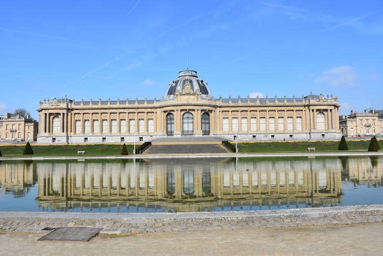 An long shot of a beige building with its reflection showing in a pool of water