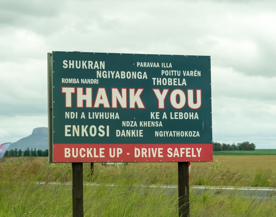 A roadside sign implores passersby to "buckle up, drive safely" in a variety of languages