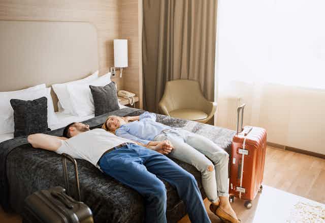 Un couple est couché, souriant, sur le dessus de lit dans sa chambre d'hôtel