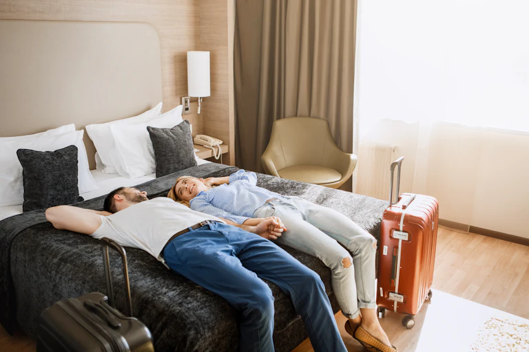 Un couple est couché, souriant, sur le dessus de lit dans sa chambre d'hôtel