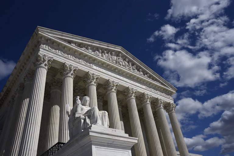 A view of the Supreme Court from the outside, with tall white pillars, against a blue sky.