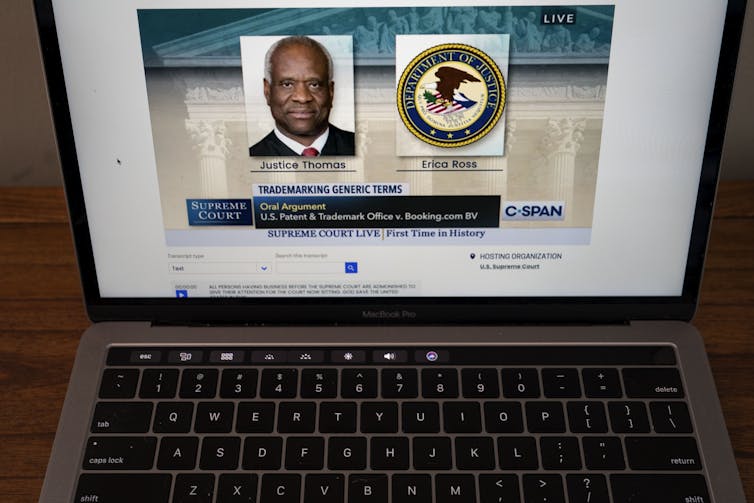A laptop screen shows an audio recording and a page that has a photo of Justice Clarence Thomas and the words 'oral arguments' regarding a trademark and patents case.
