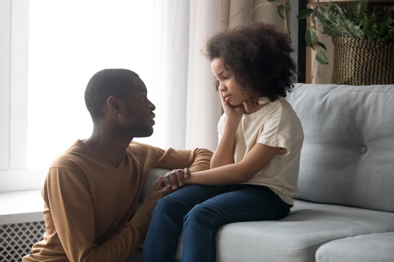 A man sitting on the floor comforting a child on a sofa