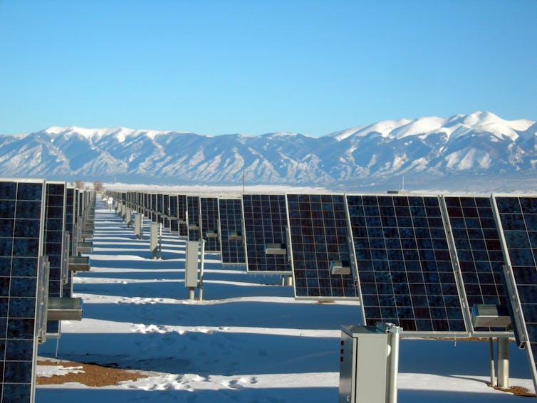 Rows of solar panels in a solar farm. Snow capped mountains in the backgrond.