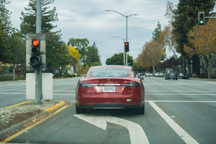 a red electric Tesla sedan stops at a traffic light