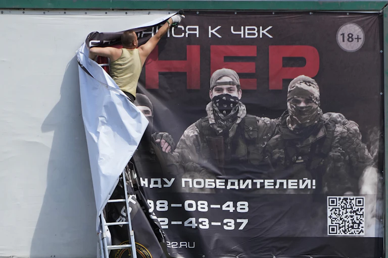A man tears down a large poster advertising the Wagner Group.