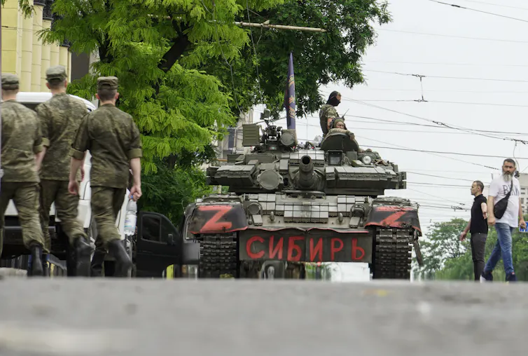 Sebuah tank di jalan kota dengan tentara dan warga sipil di sekitarnya.