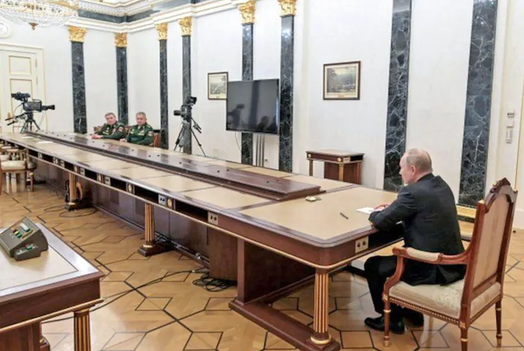 Vladmir Putin duduk bersebrangan di meja panjang dari dua pria berseragam militer.
