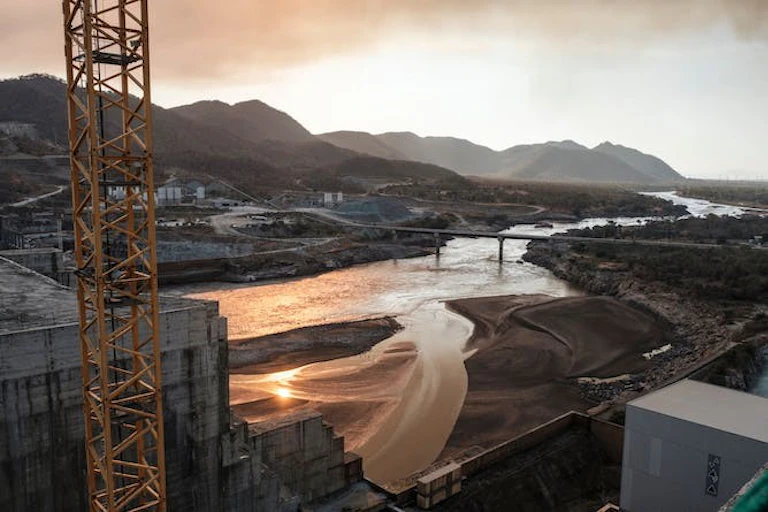 Une rivière coule sous des piliers en béton, avec une grue et des murs en béton au premier plan.