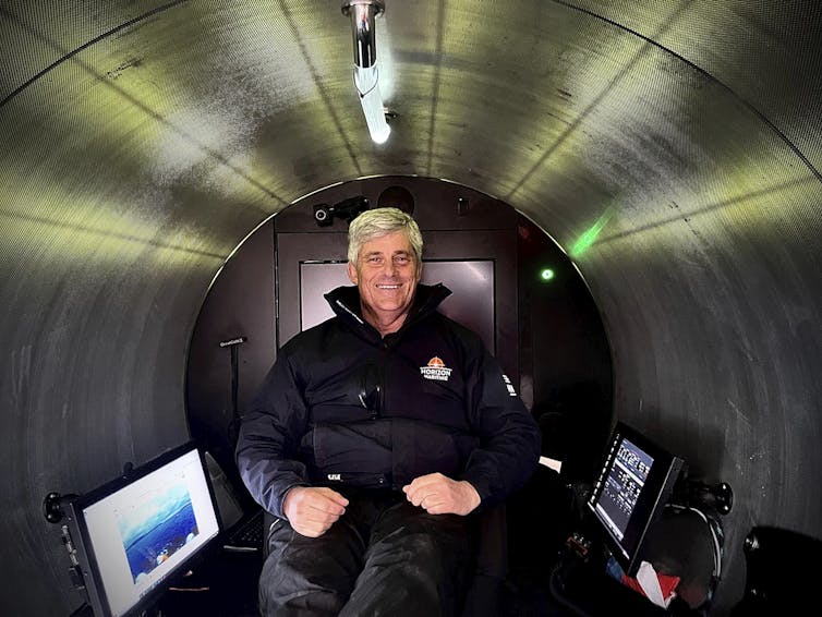 A middle-aged white man sits smiling inside of a the cylindrical body of a submersible.