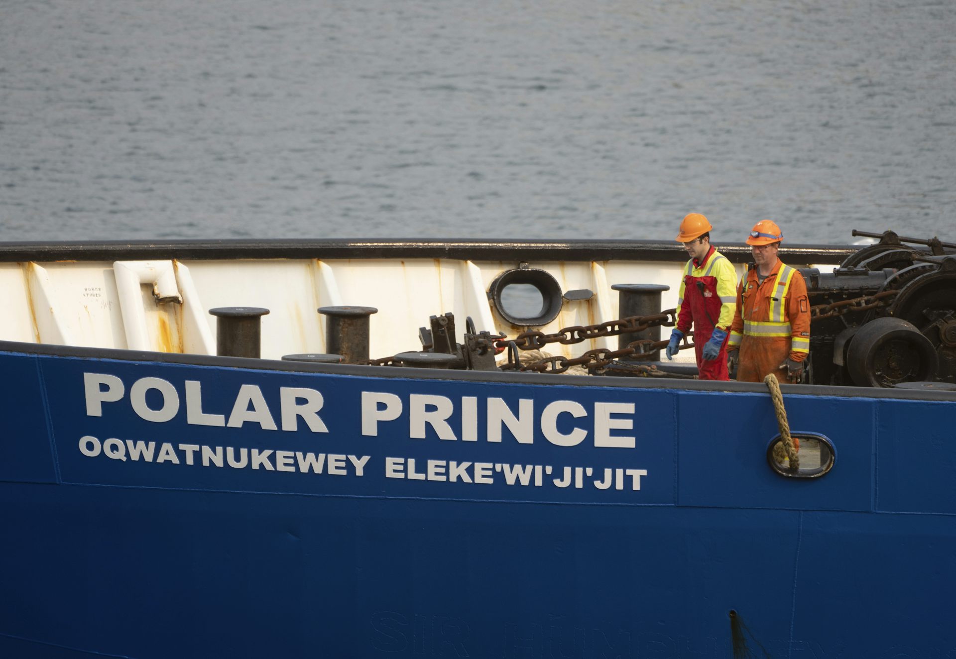 Two men in construction uniforms and hard hats stand on the bow of a large ship. The name POLAR PRINCE is written on the side of the ship.