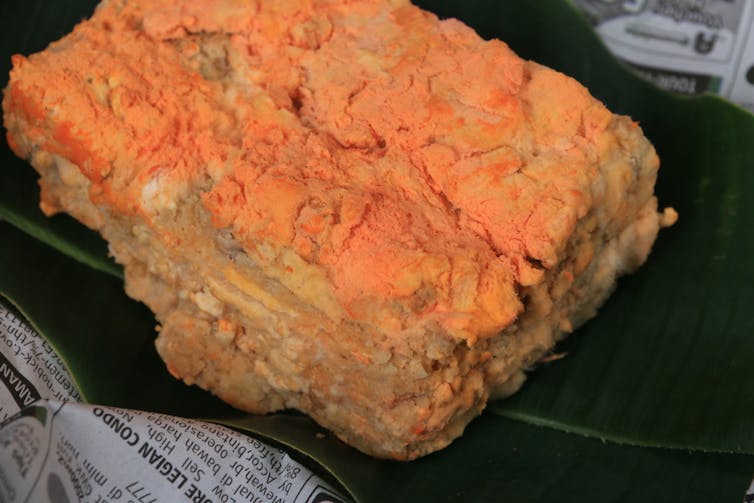 A block of orange mouldy substance sitting on a banana leaf