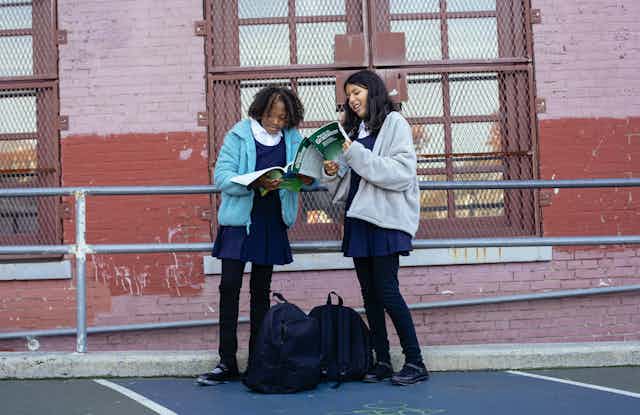 Two students look at text books in a playground. 