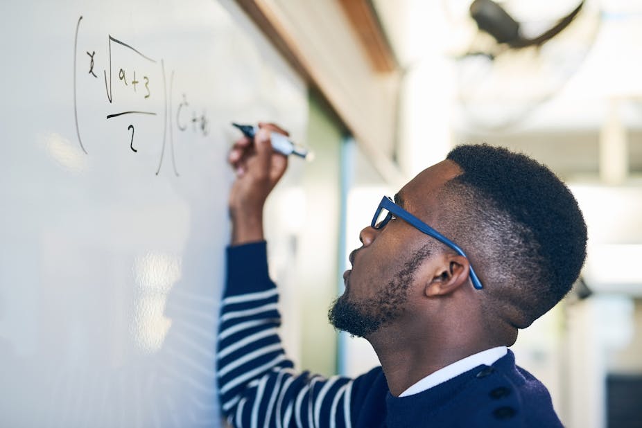 A man writes a mathematical formula on a white board in black pen