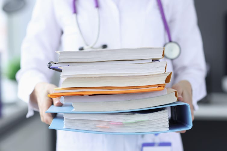 Hands of a GP holding a stack of files.