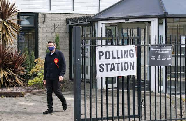 A man with a red rosette outside a polling station.