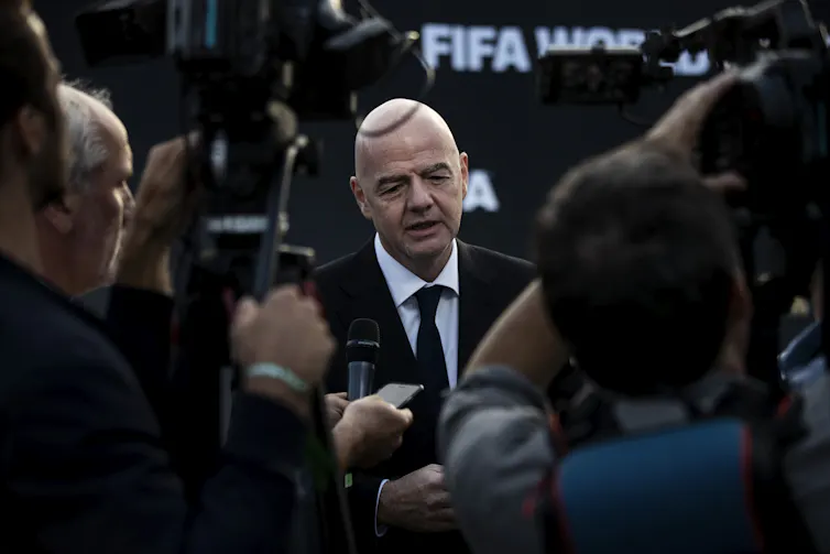 Fifa President Gianni Infantino wearing a black suit, surrounded by journalists.