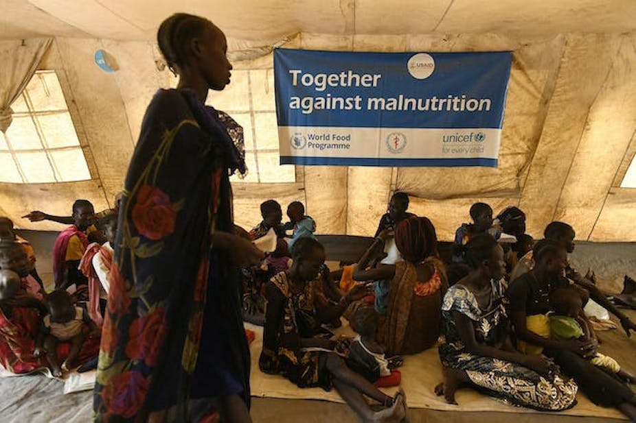 Une femme passe devant une bannière sur laquelle on peut lire "Ensemble contre la malnutrition" tandis que d'autres femmes sont assises sur le sol d'une grande tente.
