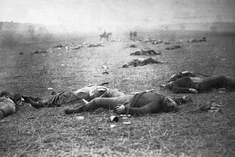 A black and white photo depicts a body-strewn field, with a person on horseback visible in the distance.