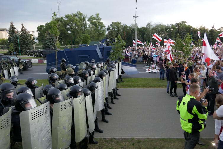 A line of riot police faces a large group of protesters.