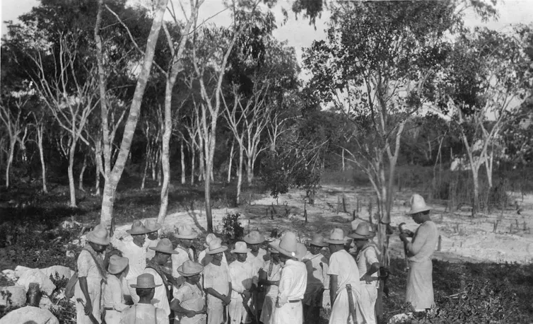 Un grupo de personas se reúne en medio del bosque en torno a otra que habla con ellos.