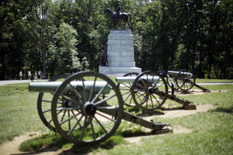 Three cannons in front of a stone monument topped with a bronze figure sitting on a horse.