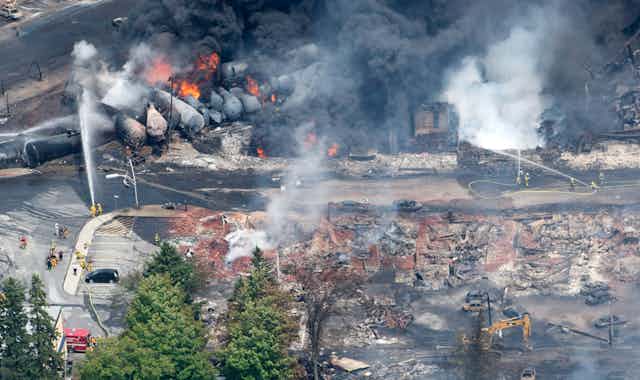 An aerial view of rail cars and a destroyed town, with smoke and flames visible.