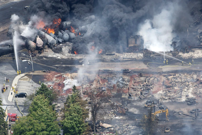 An aerial view of rail cars and a destroyed town, with smoke and flames visible.