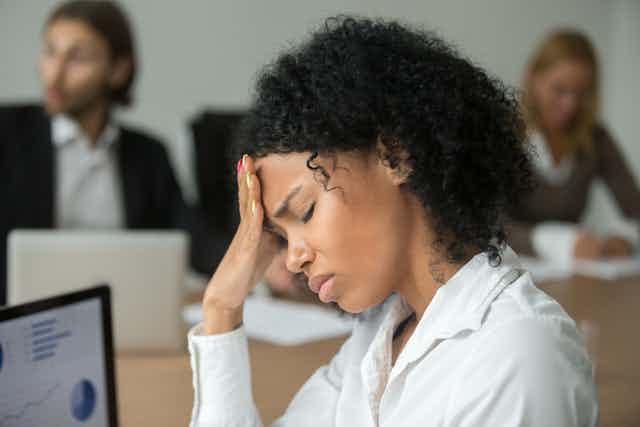 A stressed woman in an office with her hand on her forehead