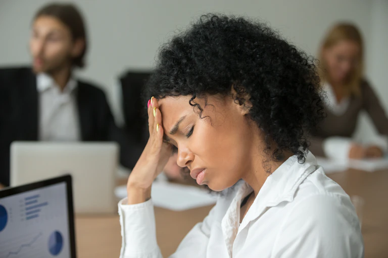 A stressed woman in an office with her hand on her forehead