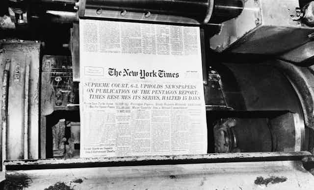 A printing press with the front page of the New York Times rolling through it.