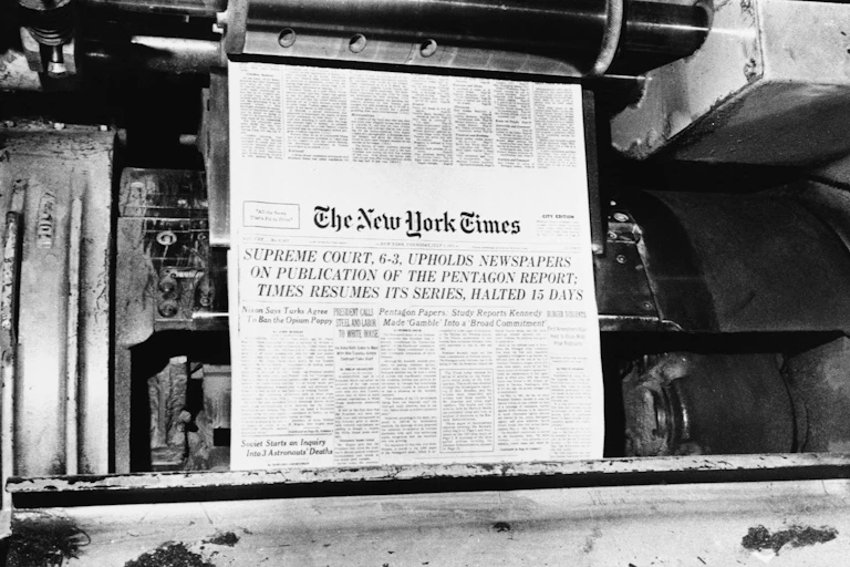 A printing press with the front page of the New York Times rolling through it.