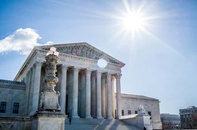 The sun beams brightly over a monumental building with tall marble pillars.