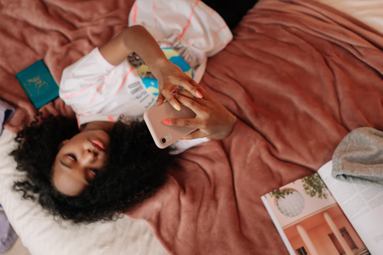 A teenager lies on her bed looking at her phone.