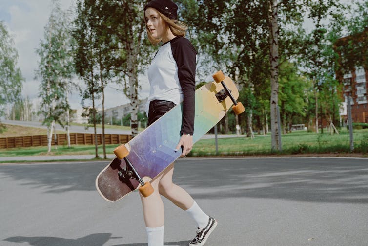 A teenager walks through a park, holding a skateboard.