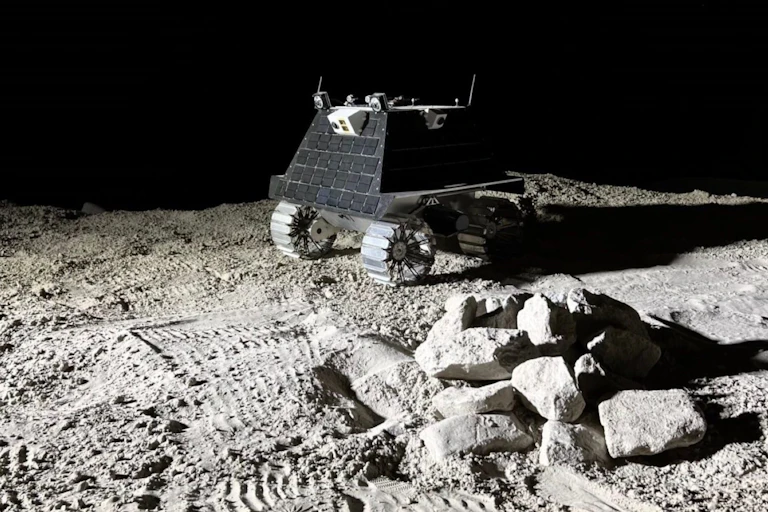A phot of a small four-wheeled robotic vehicle in a moon-like landscape