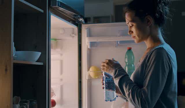 woman stands at open fridge