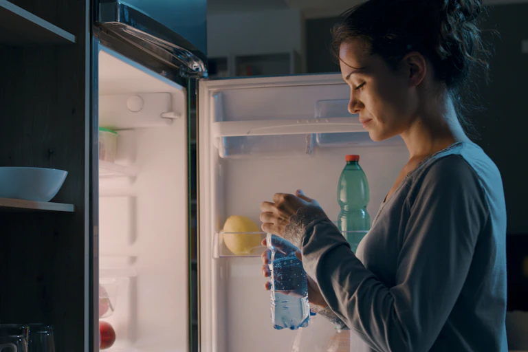 woman stands at open fridge