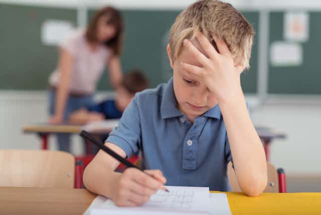 boy sits at school desk with hand on forehead