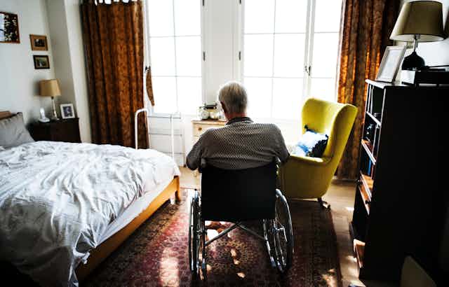 Man in wheelchair sits in bedroom