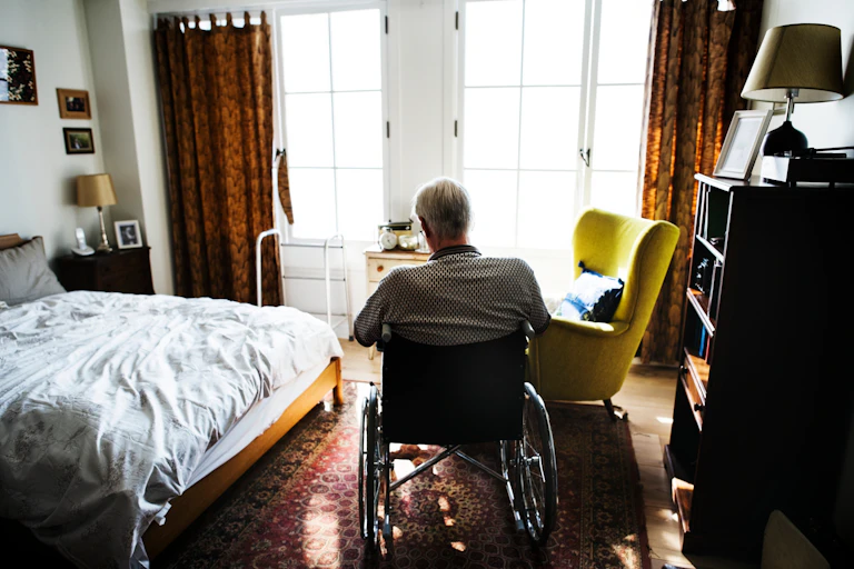 Man in wheelchair sits in bedroom