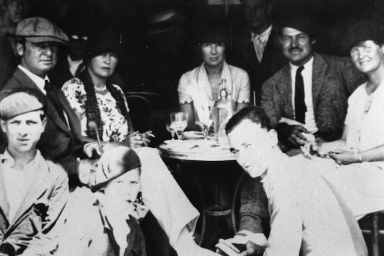 Un grupo de gente se sienta alrededor de una mesa en un bar en los años 20.
