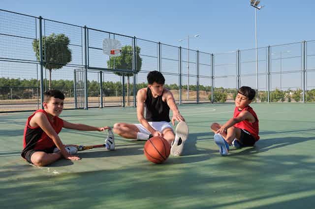 Tres niños estiran en una cancha de baloncesto, uno de ellos con una pierna ortopédica.