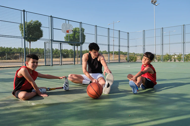 Tres niños estiran en una cancha de baloncesto, uno de ellos con una pierna ortopédica.