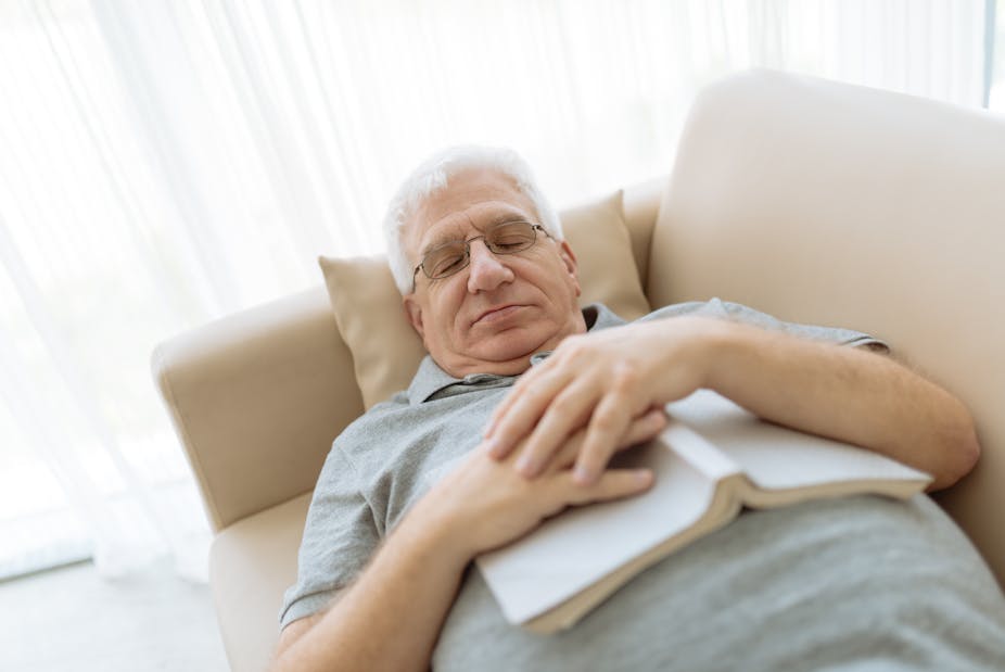 An elderly man napping on the couch with a book on his chest.