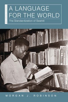 A book cover with a black and white photo of a man in a library, holding some books in one hand and reading from a book in the other.